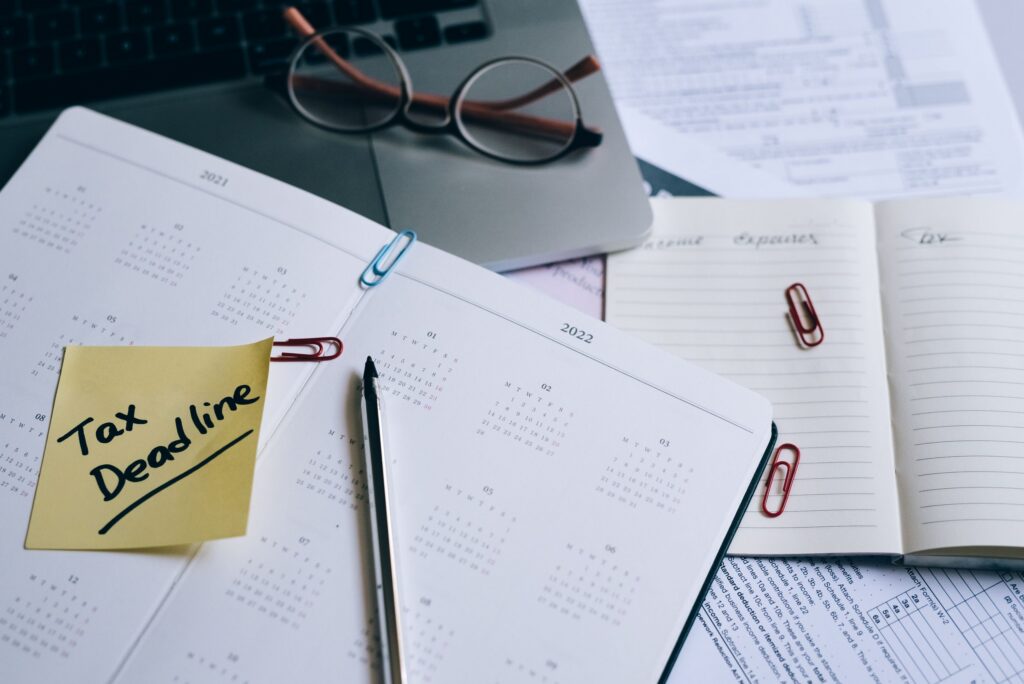 Open planner and calendar pages with a sticky note reading Tax Deadline beside eyeglasses and a laptop